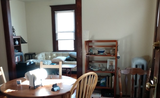 A table in the foreground, a shrine behind it, and another room peeking out from behind a doorway.