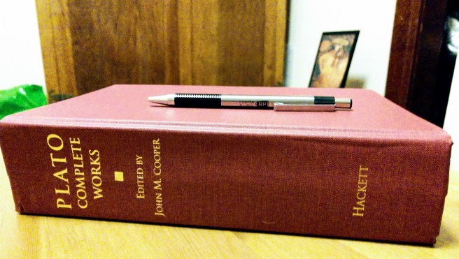 A book of Plato's complete works on its side, a pen above it. There's actually an image of Dionysos in the far background that people not using alt text would notice.