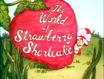 A giant strawberry with "the world of strawberry shortcake" written on it in cursive, Strawberry herself peeking out from behind it