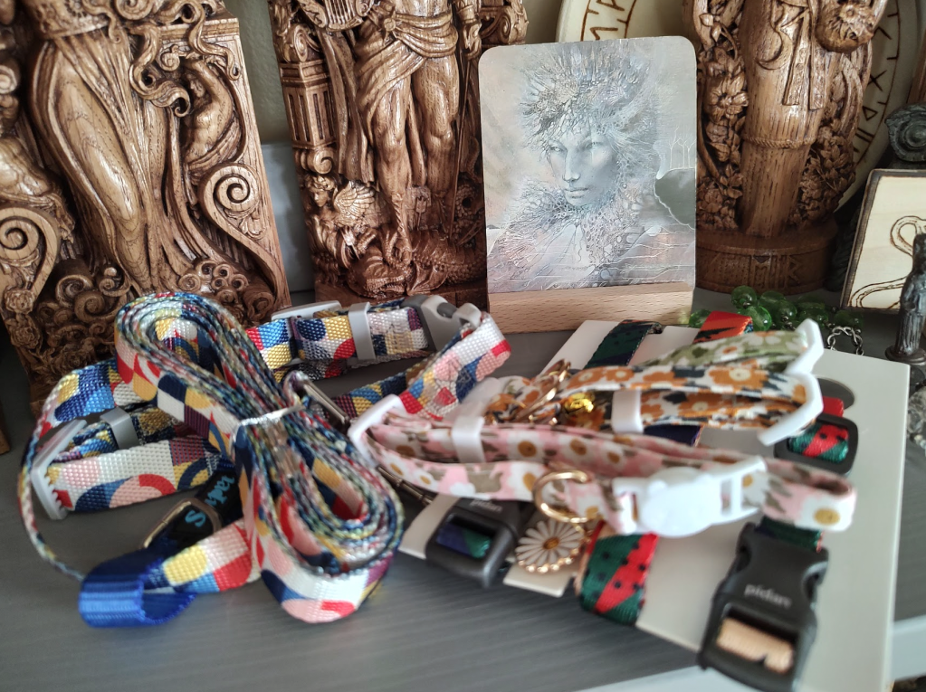 The lower bodies of several wooden statue icons in the background behind a two-dimensional card of Artemis held up by a stand. There are collars and leashes in the foreground.